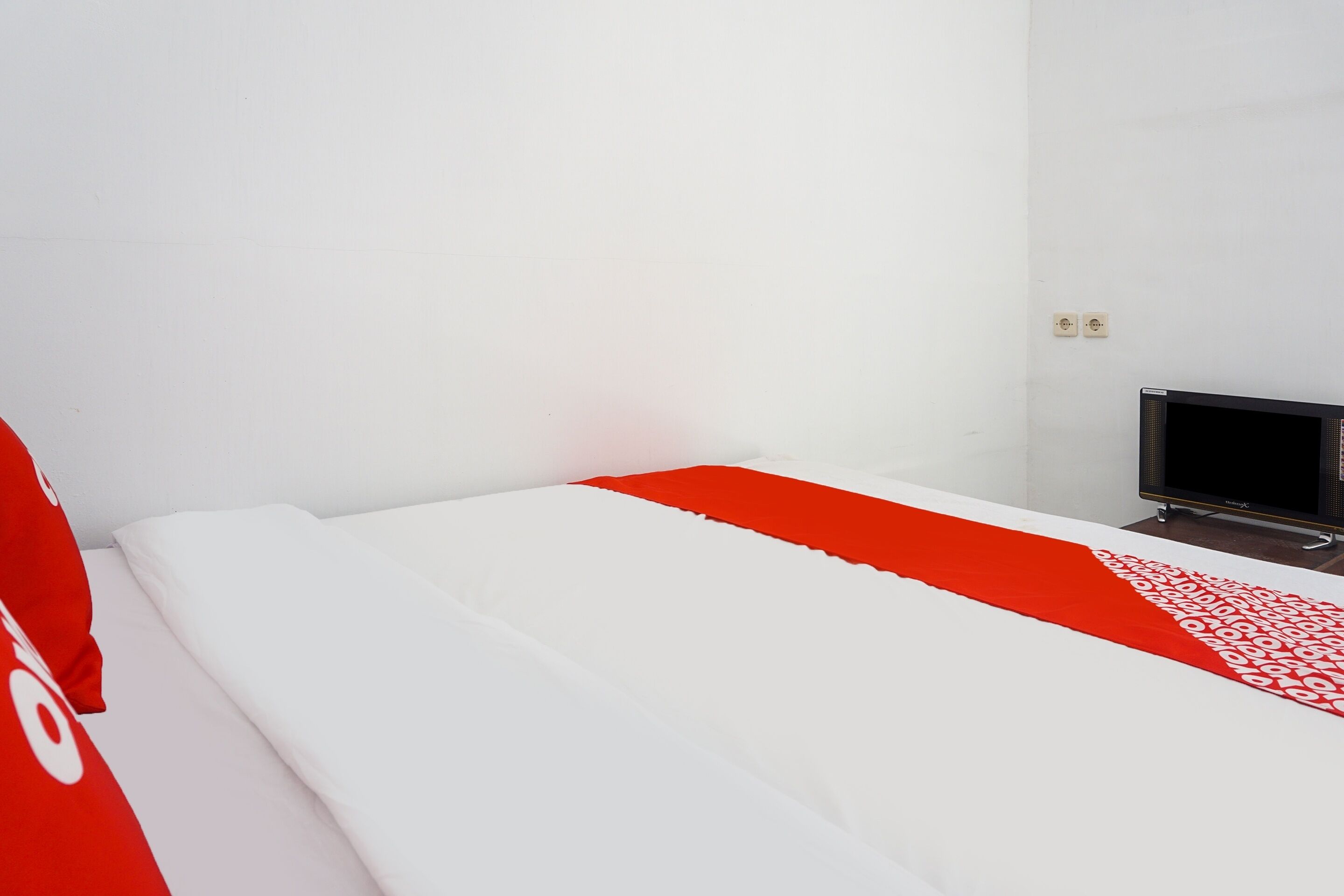 Ein Zimmer mit einem Bett, einem Fernseher und einer rot-weißen Teppichläuferdecke.