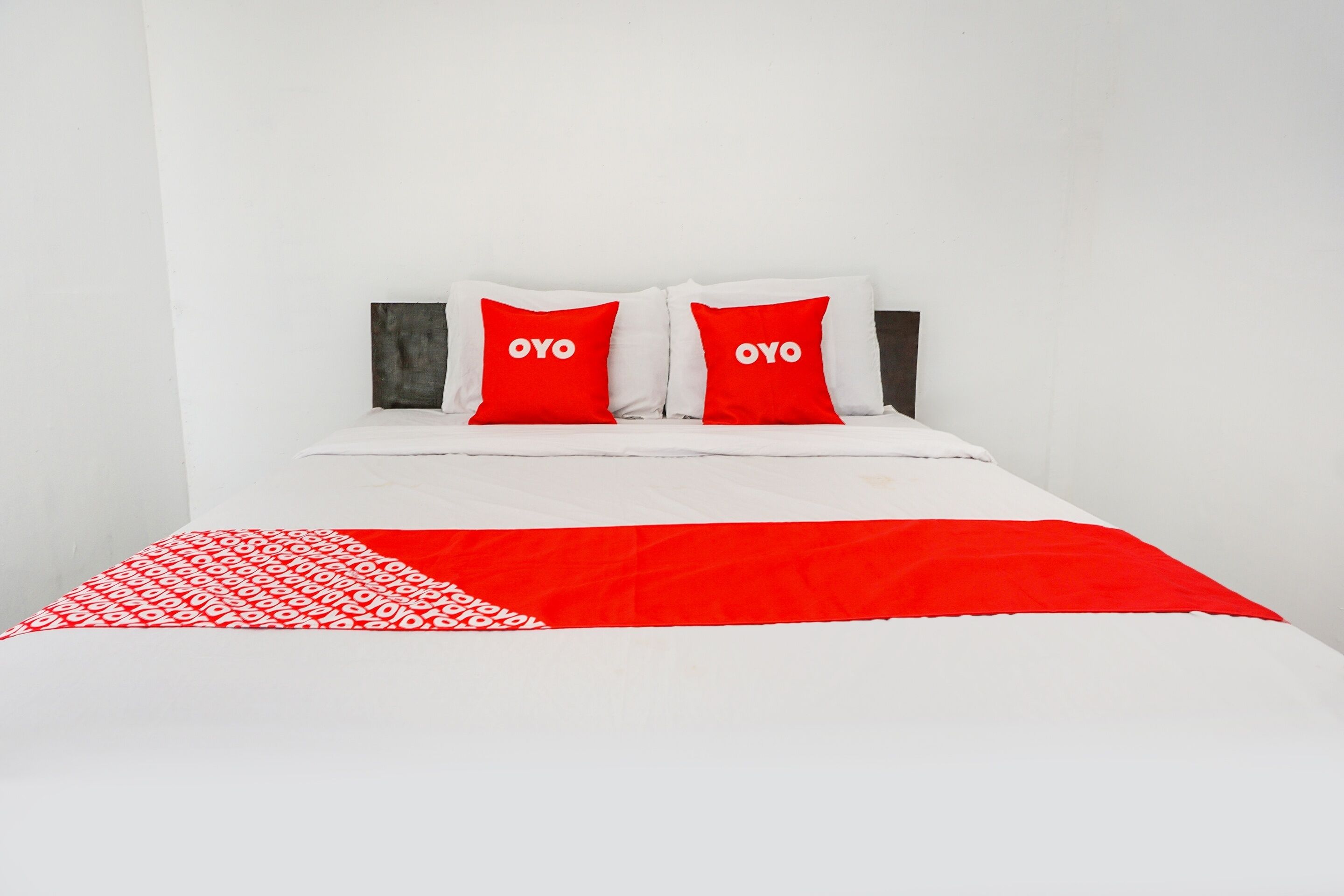 Een bed met witte beddengoed en twee rode kussens met de tekst 'OYO'.