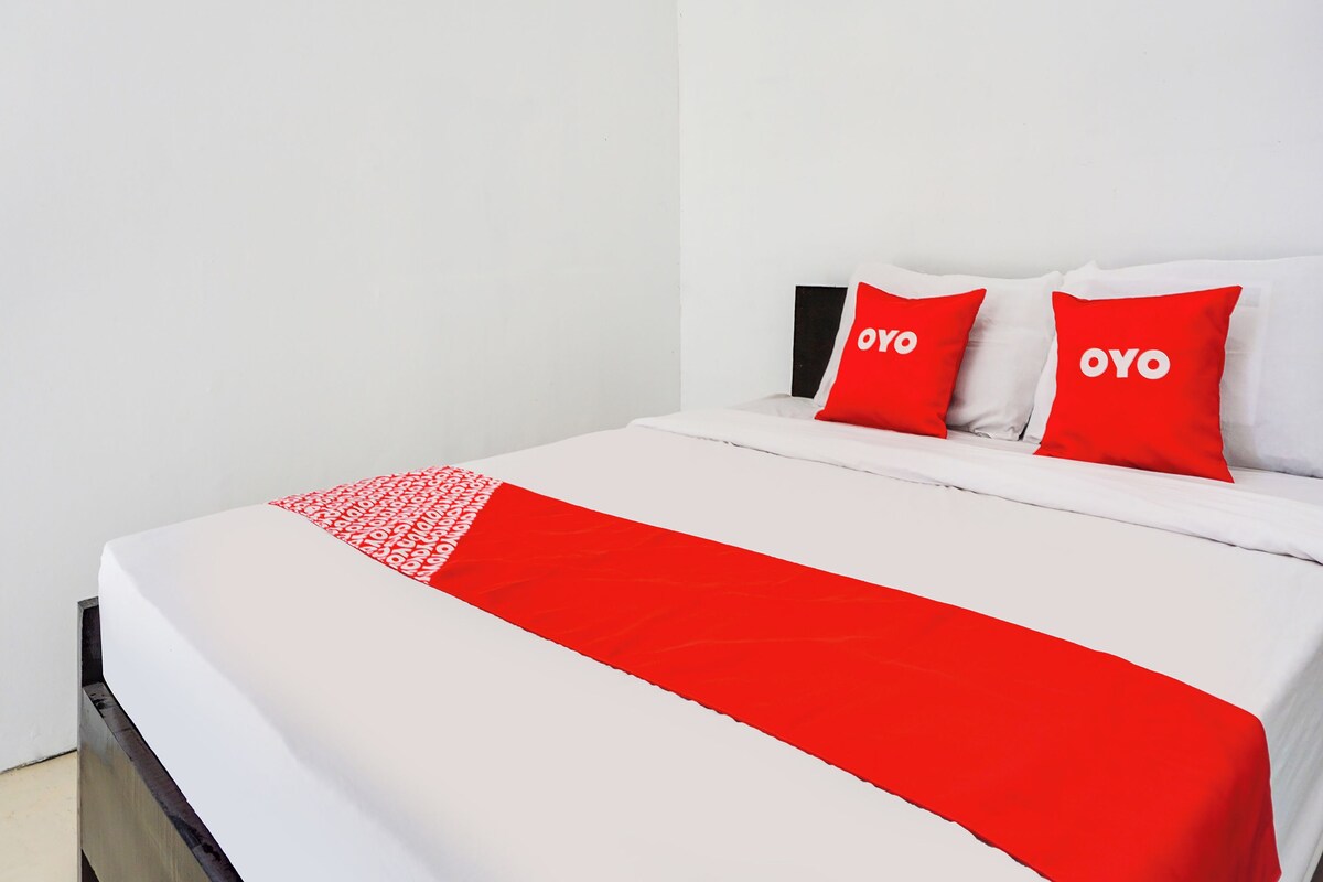 Una cama con ropa de cama blanca y dos almohadas rojas con la palabra "OYO".