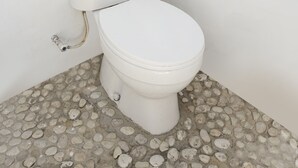 Des toilettes avec une cuvette et un abattant blancs, placées dans un coin et surmontées d’un sol dont le motif rappelle des petits galets.