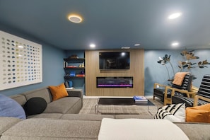 Un saló modern amb un sofà modular, un televisor de pantalla plana, una llar de foc i un panell decoratiu a la paret.