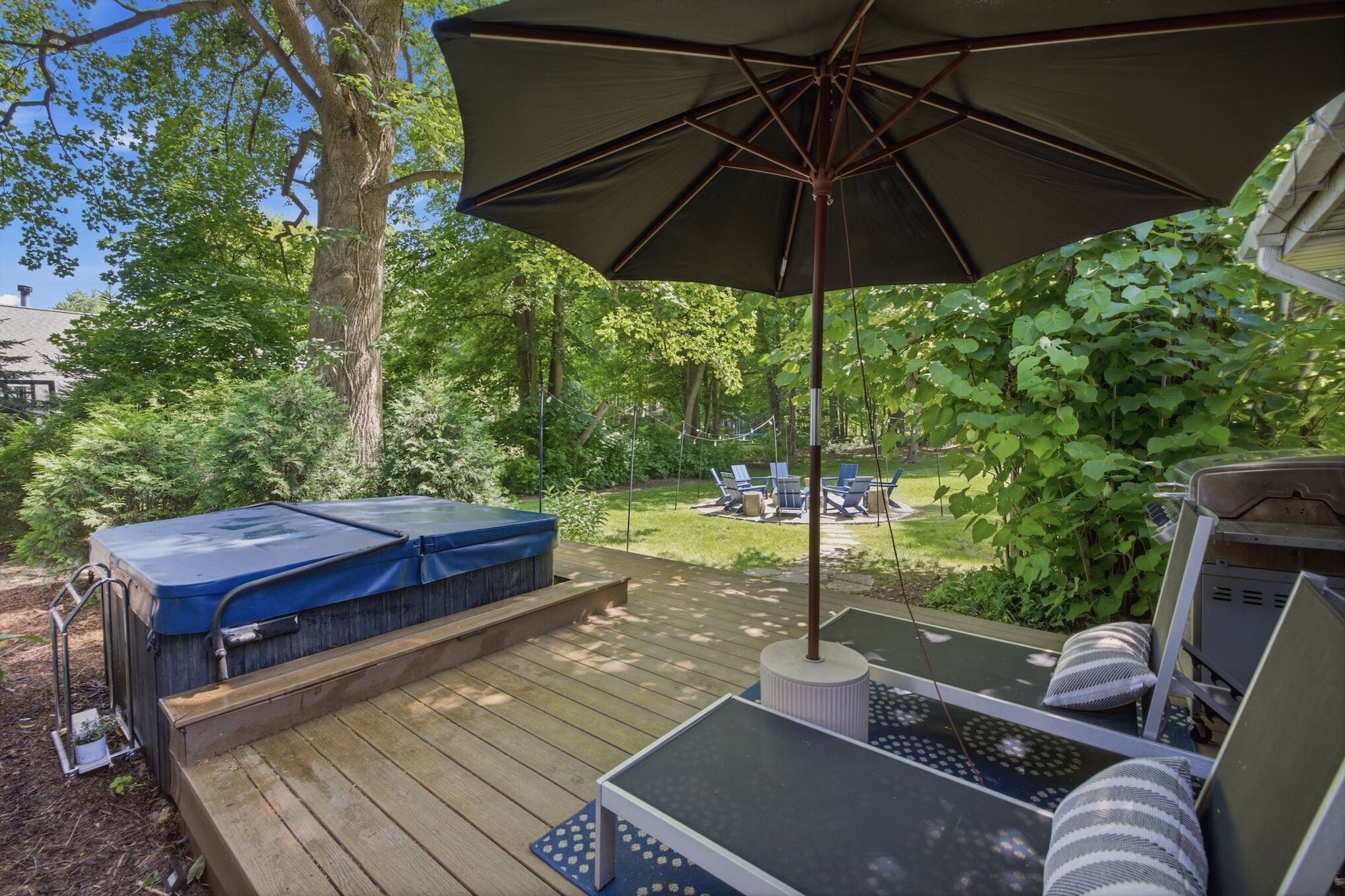 Eine Terrasse mit Whirlpool, Gartenmöbeln und einem großen Sonnenschirm.