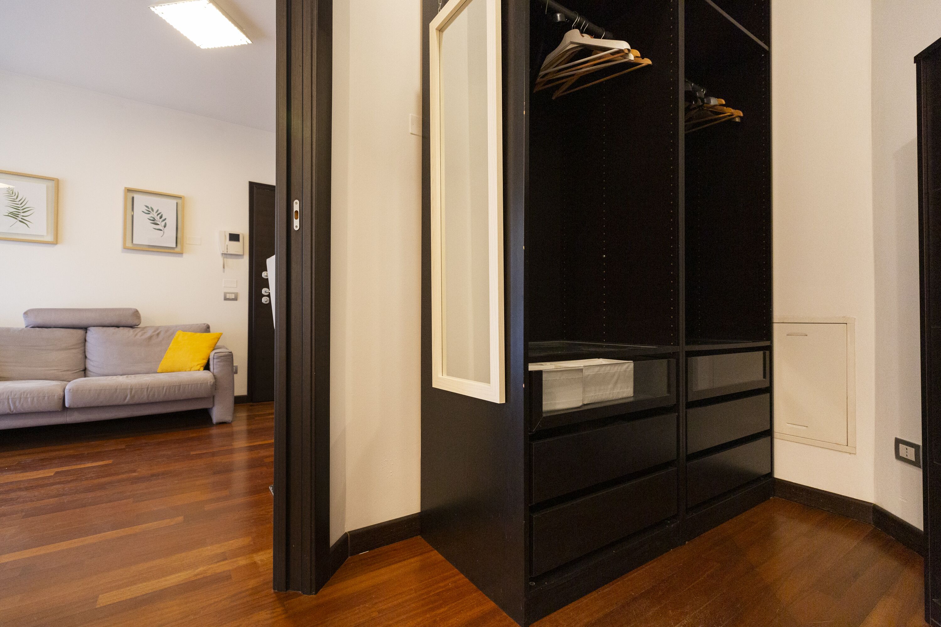 A modern room with a grey sofa, a black wardrobe, and wooden flooring.