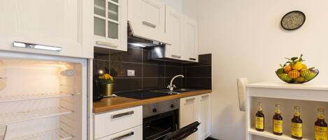 A kitchen with white cabinets, a black backsplash, a wooden countertop, and a shelf with bottles.