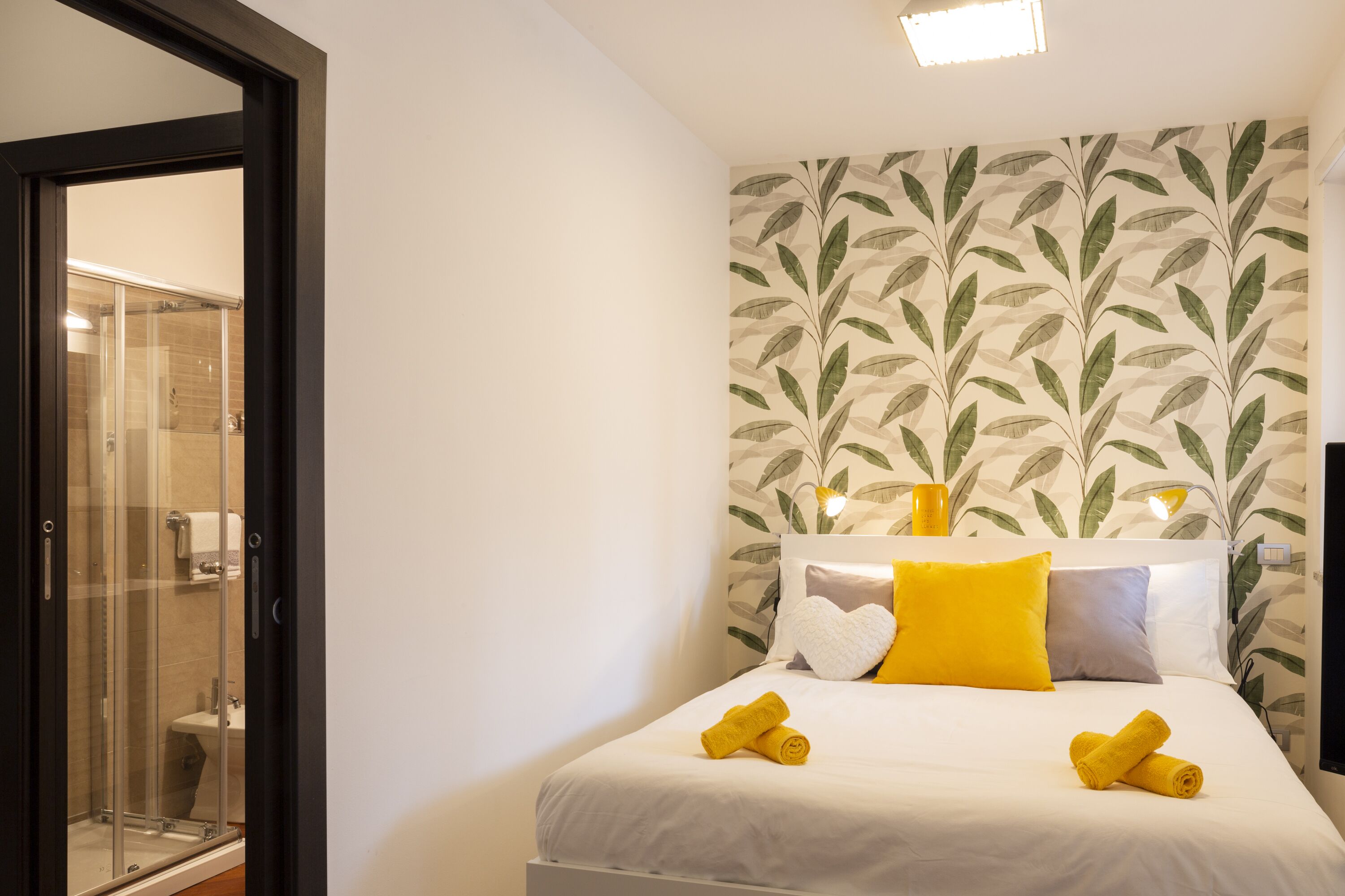 A hotel room with a bed, a shower area, and a wall with a leaf pattern.