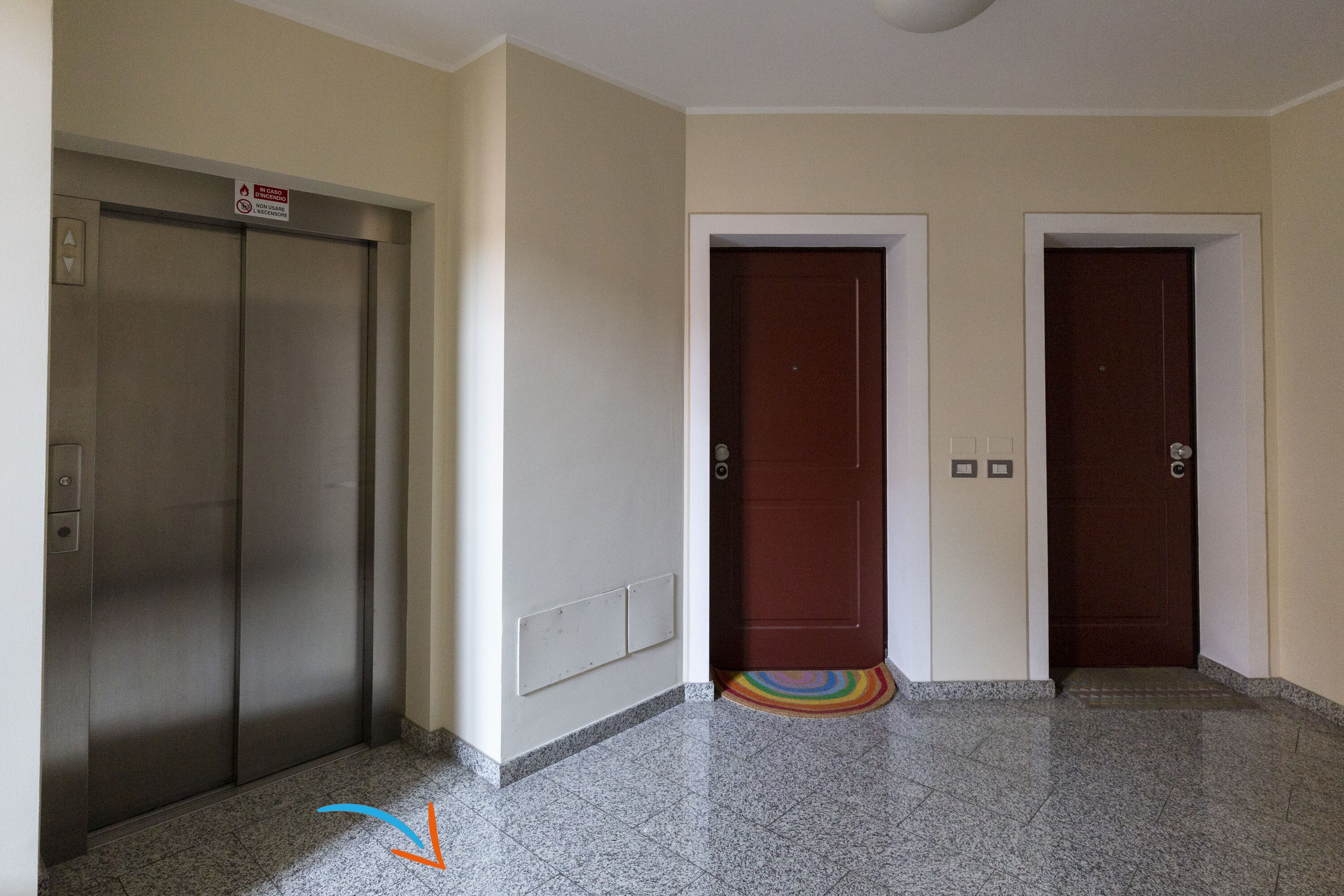 An elevator, two wooden doors, a tiled floor, and a colorful rug.
