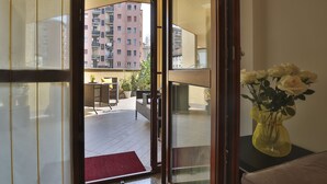 Une pièce avec vue sur un balcon, un tapis rouge et un vase jaune orné de fleurs.