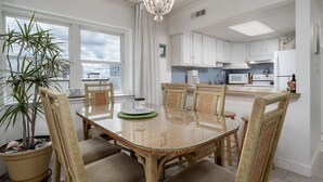 A modern kitchen with white cabinets, a glass dining table, wicker chairs, and a potted plant. - Beautiful two bedroom, 2 bath condo in desirable North OC with great views! (Ocean City)