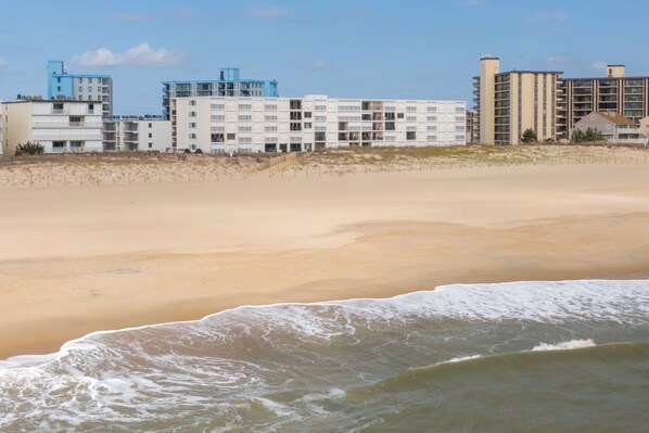Un hotel frente a la playa con varias construcciones, playa de arena y olas marinas.