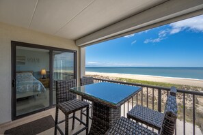 Un balcón con mobiliario de mimbre, una mesa de vidrio y vista a la playa.