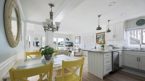 A bright kitchen with white cabinets, a dining table with yellow chairs, and a large mirror on the wall.