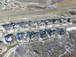 Vista aérea de una zona residencial con casas alineadas a lo largo de una carretera, rodeada de terreno abierto y una autopista al fondo.