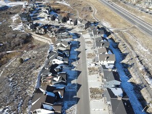 Vista aérea de una zona residencial con casas alineadas a lo largo de una carretera, rodeada de terrenos abiertos y una autopista.