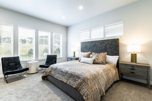 Un dormitorio moderno con una cama grande, dos mesitas de noche, una silla y una pequeña mesa redonda.