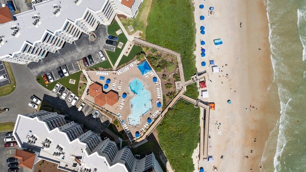 An aerial view of a hotel with a swimming pool, beach umbrellas, and a beach area.
