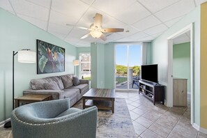 A living room with a sofa, coffee table, and armchair, a television, and a ceiling fan.
