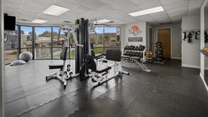A gym with various exercise equipment, a wall-mounted dumbbell rack, and a large window offering a view of the outdoors.