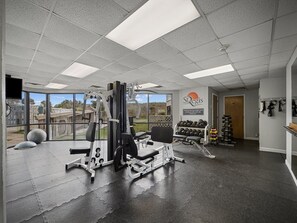 A gym with various exercise equipment, a wall-mounted dumbbell rack, and a large window offering a view of the outdoors. - St. Regis 3012- 3BR Oceanfront Condo in North Topsail Beach with Tennis Court, Elevator & Communi... (North Topsail)
