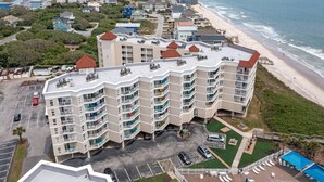 A multi-story hotel with balconies, a parking lot, and a beach view.