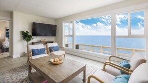 Un ampio soggiorno con una grande finestra vista oceano, una TV a schermo piatto montata a parete e un tavolino da caffè in legno.