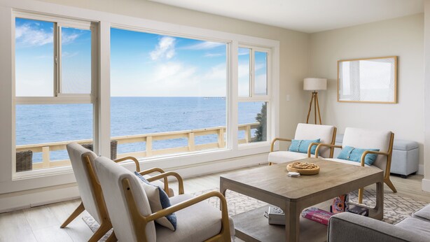 Una stanza con ampie finestre vista mare, un tavolo di legno e due divani.