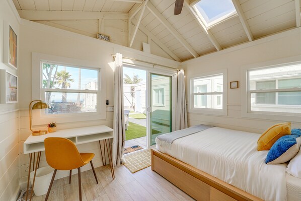 A bedroom with a bed, desk, chair, and large windows.