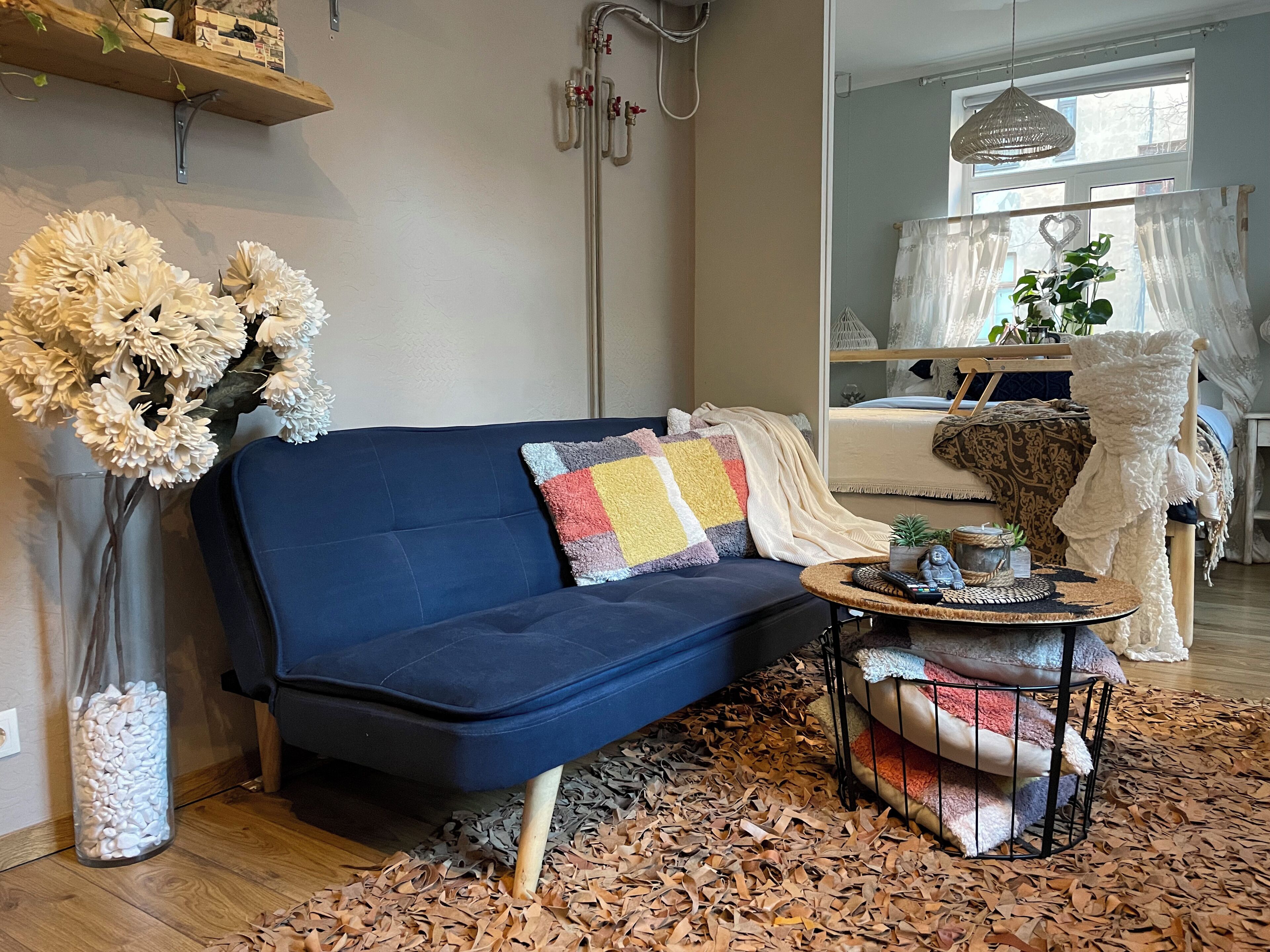 A cozy living room with a dark blue sofa, a round coffee table, and a large vase of white flowers.
