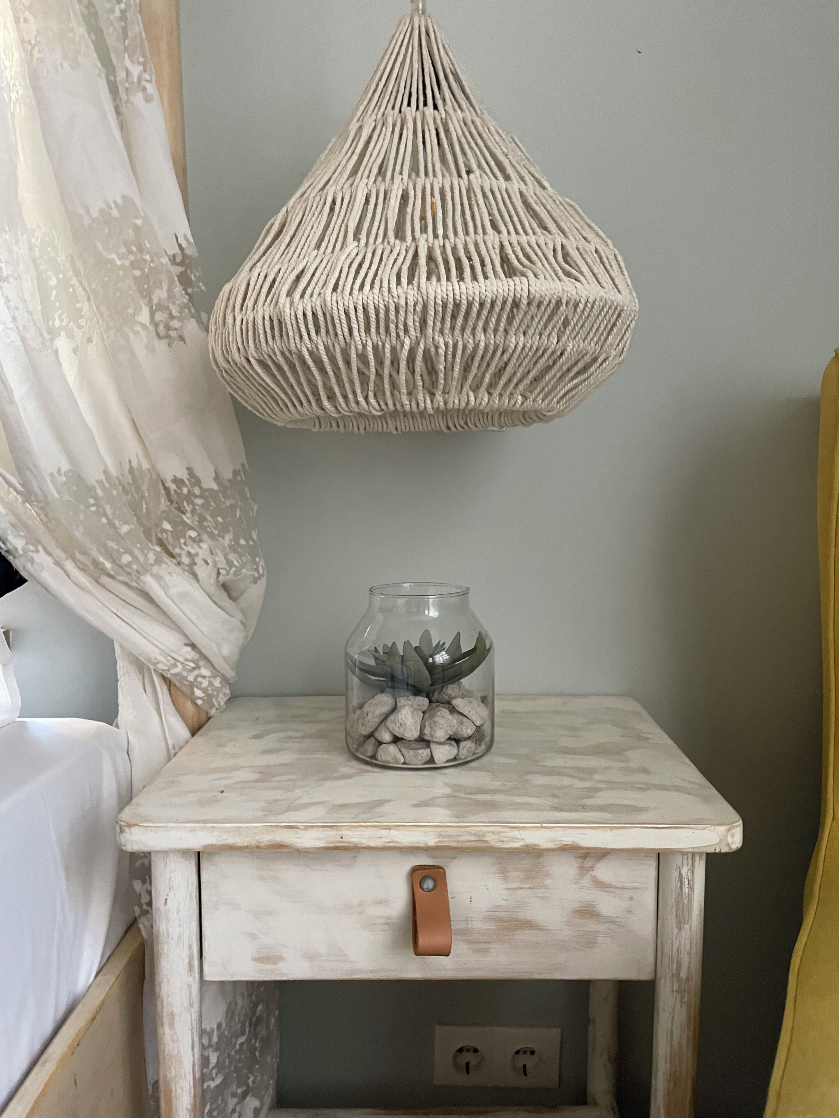A small, rustic bedside table with a glass jar containing rocks and a succulent plant.