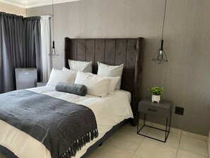 A modern bedroom with a large bed, a bedside table with a plant, and a small cabinet. - Loft Bella Vita (Bloemfontein)