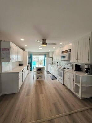 A modern kitchen with white cabinets, a ceiling fan, and a view to the outside.