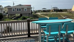 Une terrasse avec une table et des chaises, donnant sur une plage et des maisons.