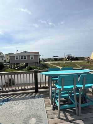 A deck with a table and chairs, overlooking a beach and houses.