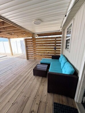 Un espace extérieur aménagé avec une terrasse en bois, un canapé avec des coussins bleus et un pouf en osier.
