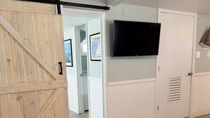 Une pièce avec une porte en bois, un téléviseur fixé au mur et un tapis à motifs sur le sol.