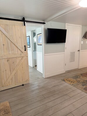 A room with a wooden door, a television mounted on the wall, and a patterned rug on the floor.