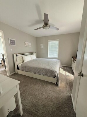 A bedroom with a bed, a ceiling fan, a window, and a door.