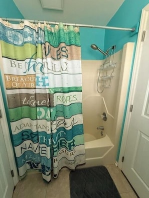 Une salle de bain avec un rideau de douche orné de motifs et d’inscriptions sur le thème de la marine, une baignoire et un petit tapis noir.