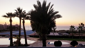 Un complexe hôtelier doté d’une piscine, de palmiers et offrant une vue sur la mer au coucher du soleil.