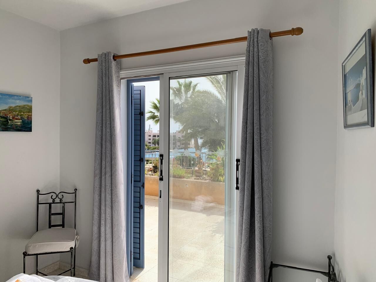 Una habitación con una cama, una silla, un ventanal corredero con cortinas y vistas al exterior.