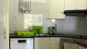 Une cuisine compacte avec des meubles blancs, un lave-vaisselle, une bouilloire et une horloge au mur.