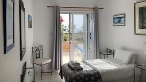 Une chambre à coucher comprenant un lit, une chaise, une table de chevet, un ventilateur de plafond et une vue sur l’extérieur.