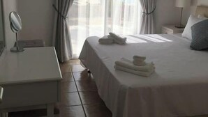 Ein Hotelzimmer mit Bett, Nachttisch mit Lampe, einem Fenster mit Vorhängen und einem Spiegel an der Wand.