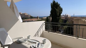 Ein Balkon mit Tisch für zwei Personen, mit Blick auf die Küste, Gebäude und einen hohen Baum.