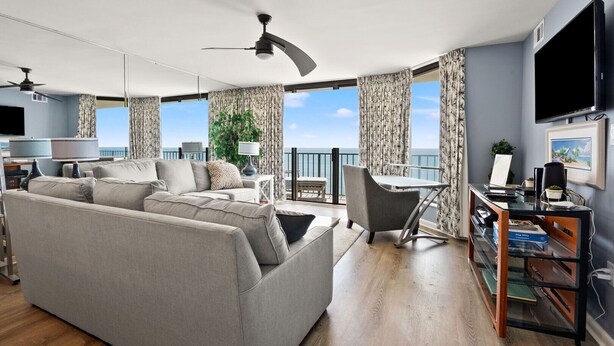 Ein modernes Wohnzimmer mit einer Couch, einem Essbereich mit Tisch und Stühlen, einem Fernseher und einem Balkon mit Vorhängen.
