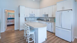 A modern kitchen with white cabinetry, a central island with bar stools, a built-in microwave, and a double-door refrigerator. - Beautiful Bayfront Townhouse located downtown Ocean City. Free WiFi, Elevator (Ocean City)