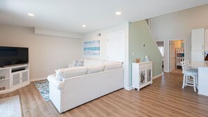 A living room with a white sofa, a flat-screen TV, and a dining area with a white table and chairs. - Beautiful Bayfront Townhouse located downtown Ocean City. Free WiFi, Elevator (Ocean City)
