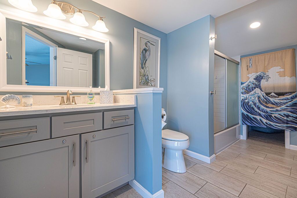 A bathroom with a large mirror, a toilet, a shower, and a sink with a vanity.