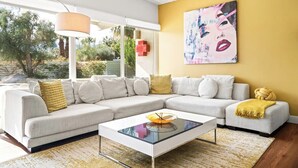 Un salon moderne avec un canapé d’angle, une table basse en verre et un mur d’accent jaune.