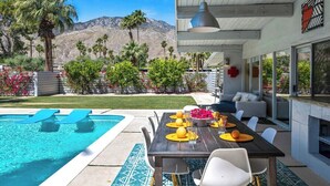 Un espace repas aménagé au bord de la piscine, avec une table dressée pour quatre personnes, une piscine et une vue sur les montagnes.