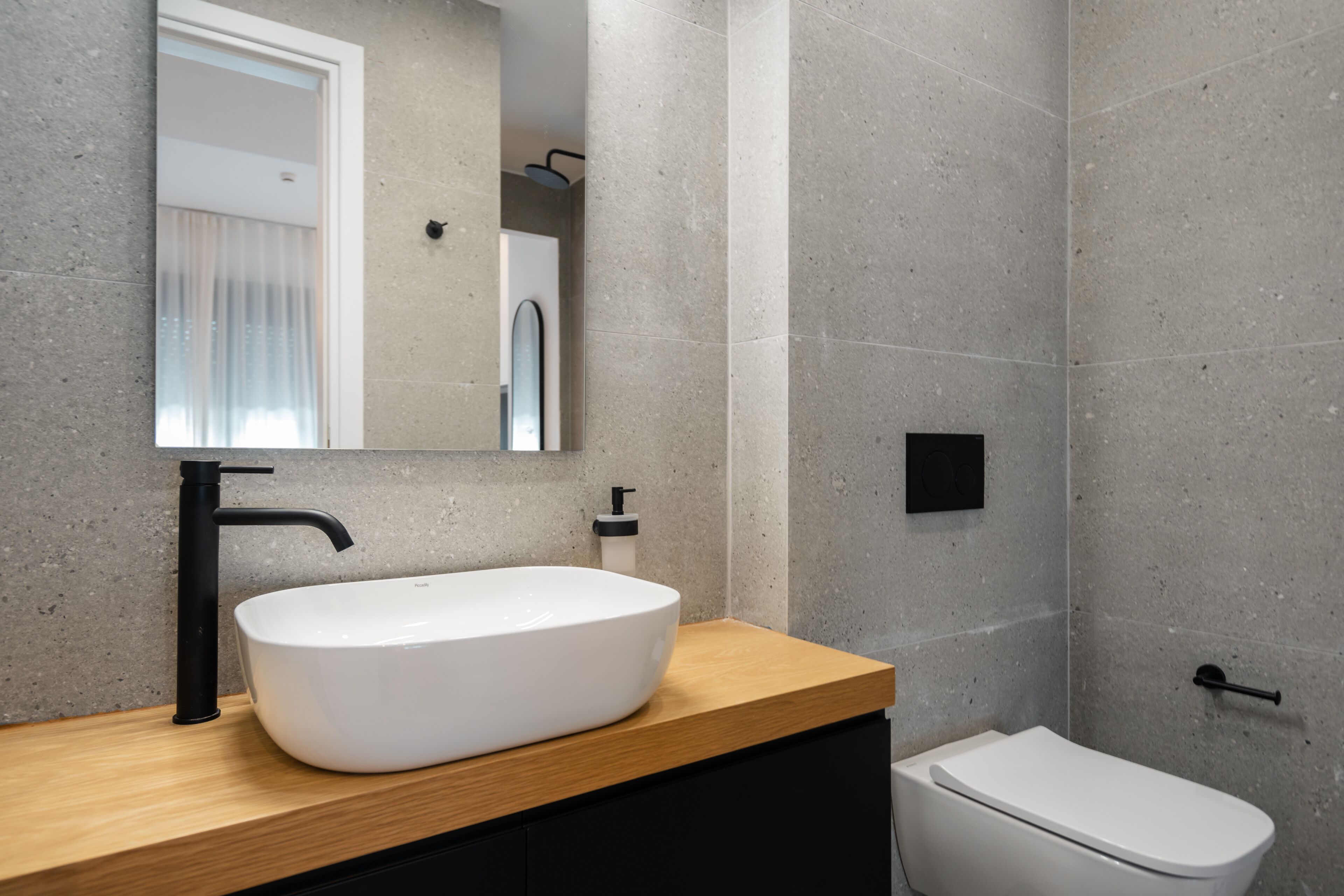 Une salle de bain moderne avec un lavabo sur colonne blanc, un robinet noir et un plan de toilette en bois.